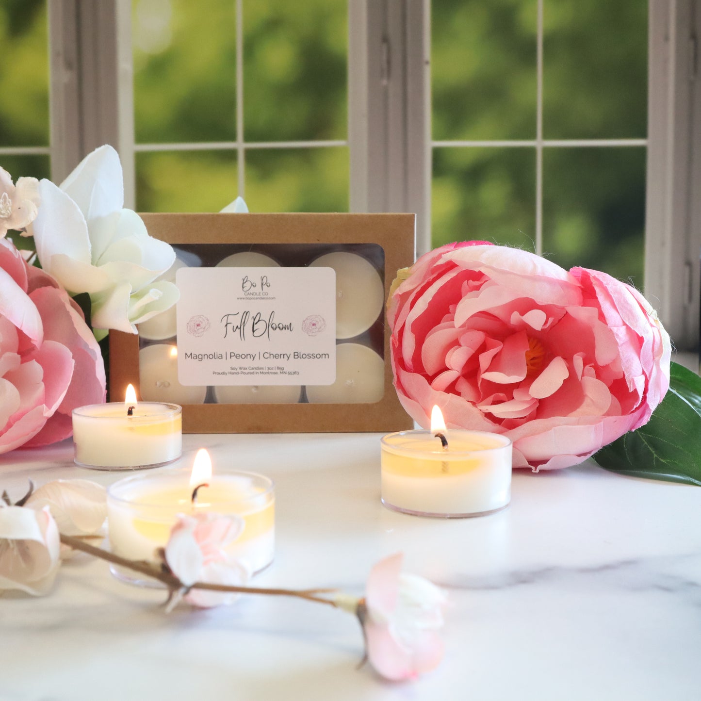 Candle set with floral packaging and pink flowers on a marble surface.